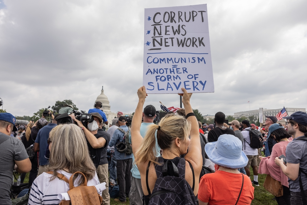  Девушка держит плакат с надписью «Коррупционная сеть», аббревиатура которой составляет название телекомпании CNN. Внизу надпись «Коммунизм – другая форма рабства». Вашингтон, США.  