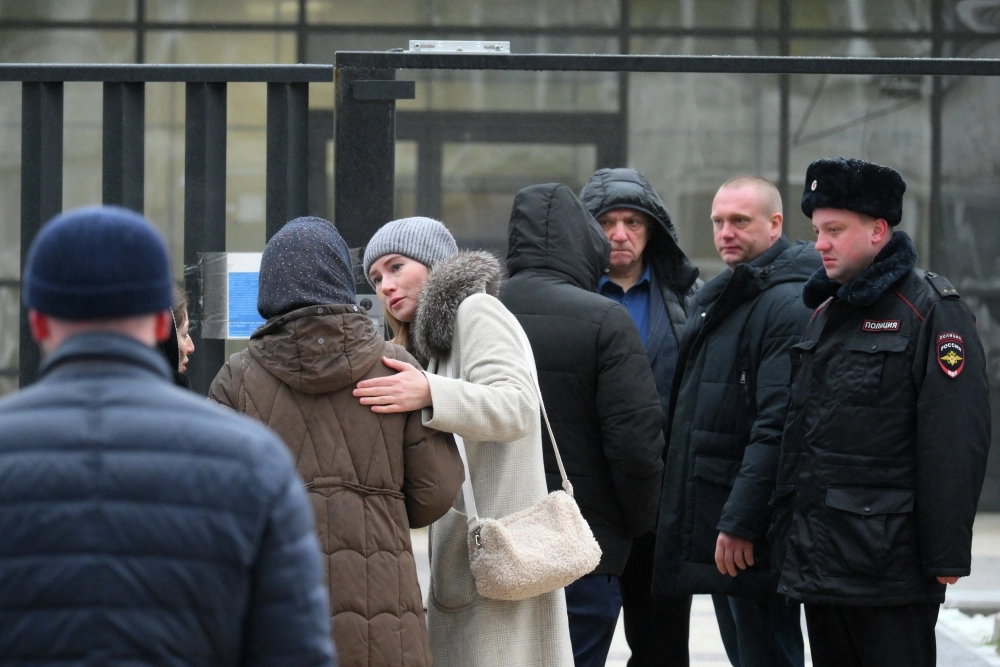 В коричневой куртке предположительно мама убитого мальчика. Обстановка возле Успенской школы в поселке Горки-2 Московской области. 