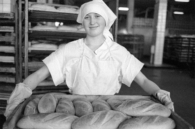 Укладчица кондитерско-булочного комбината «Черемушки» держит в руках лоток свежеиспеченного хлеба. 1983 г.