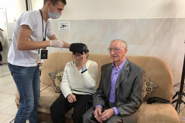 Сотрудник геронтологического центр помогает пожилой паре отправиться в виртуальное путешествие