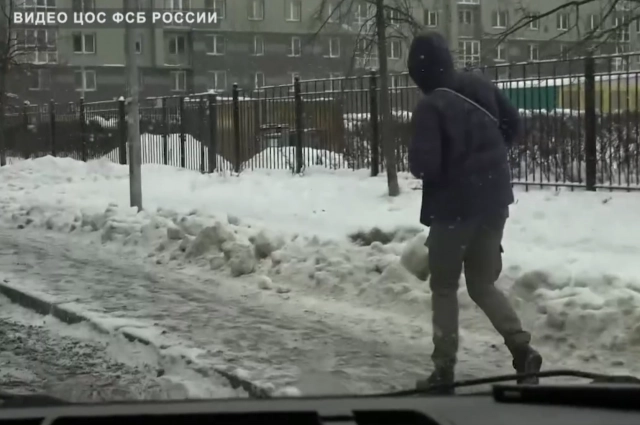 Наёмник буднично идёт к дому вероятной жертвы, не подозревая, что за ним наблюдают из машины.