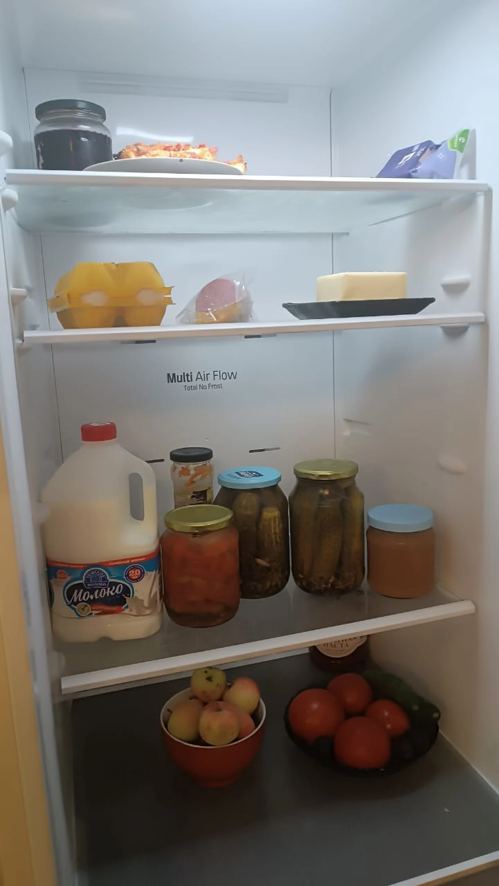 В холодильнике Виталия Титова: верхняя полка — вишнёвое варенье, пицца, сыр, вторая полка — яйца, варёная колбаса, сливочное масло, третья полка — молоко, солёные огурцы и помидоры, яблочное повидло, четвёртая полка — яблоки, помидоры.