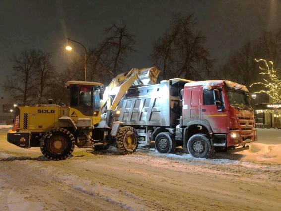 Погрузчик загружает снег в самосвал