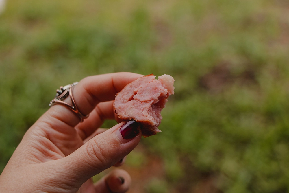 Девушка пробует полукопченую колбасу на вкус.