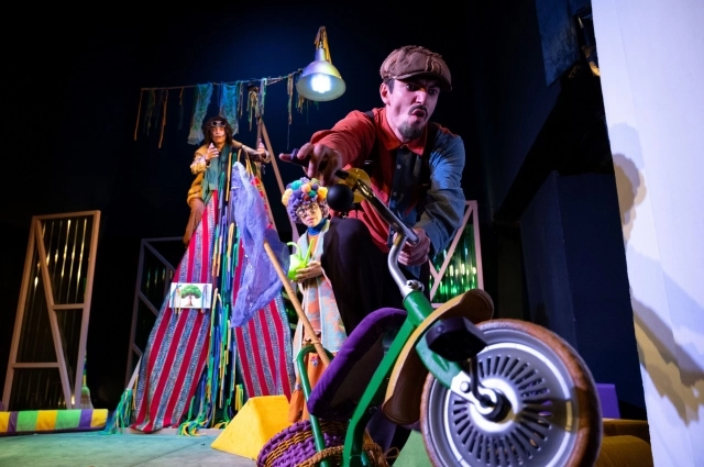 Разбойник въезжает на сцену на детском трёхколёсном велосипеде.