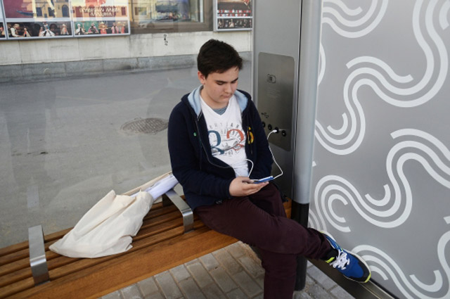 Молодой человек заряжает телефон на автобусной остановке. 