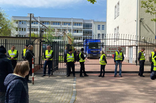 Представители мэрии в сопровождении полиции стоят возле ворот школы при российском посольстве в Варшаве.