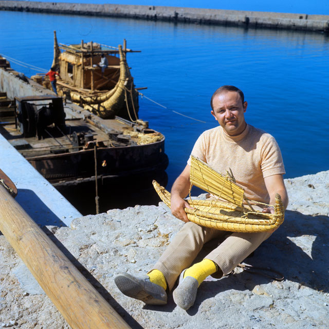 Юрий Сенкевич, врач, член интернационального экипажа папирусной лодки «Ра-2», с макетом лодки в руках. На заднем плане — папирусная лодка.