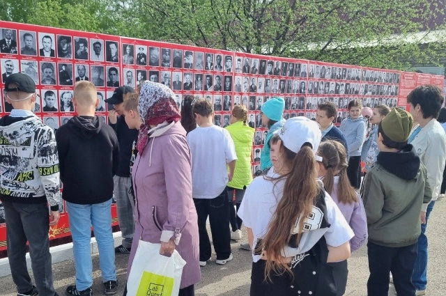 Жители смотрят на портреты ветеранов ВОВ, размещенные на Стене памяти.